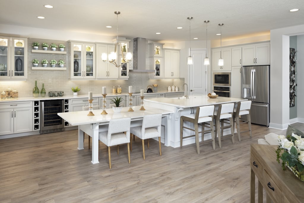 Open concept kitchen with white cabinets and white island, with many pendant and recessed lights